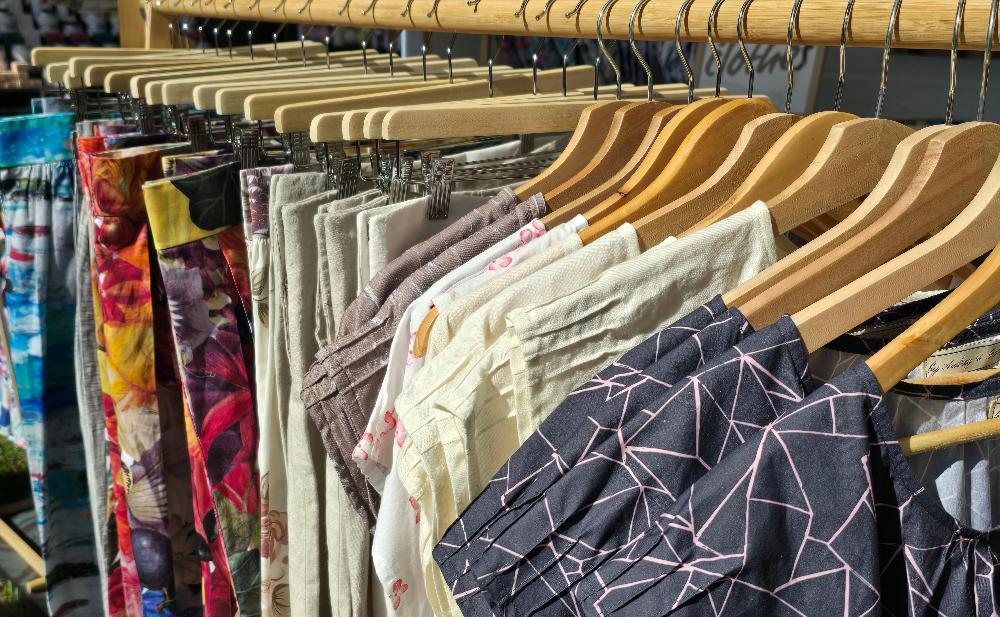 We can see a close up of o wooden rack of clothing with by Audrey and Grace Zero waste tops and zero waste skirts hanging from wooden coat hangers